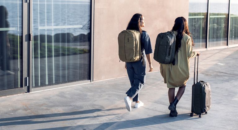 Two women walk down a city street in the sunset with Thule Aion backpacks and a Thule Aion suitcase.