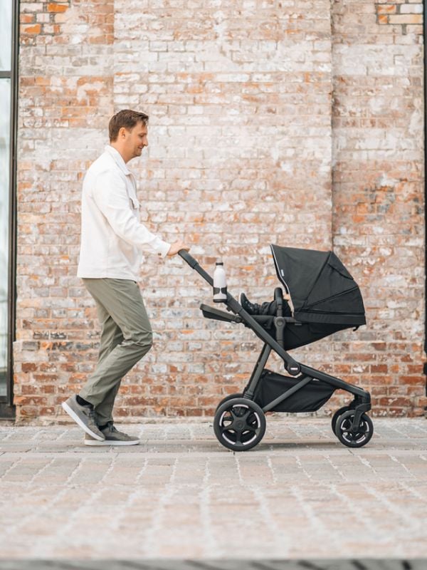 Un hombre camina con un cochecito Thule Sleek 2 en color negro