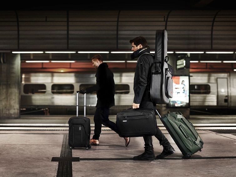 Two men walk down the platform of a train station with Thule Crossover luggage and a briefcase. 