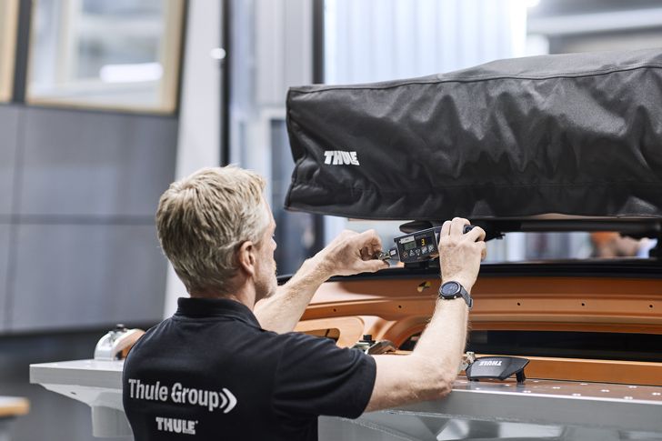 At the Thule Test Center, a man is using a tool to check something on a Thule rooftop tent.