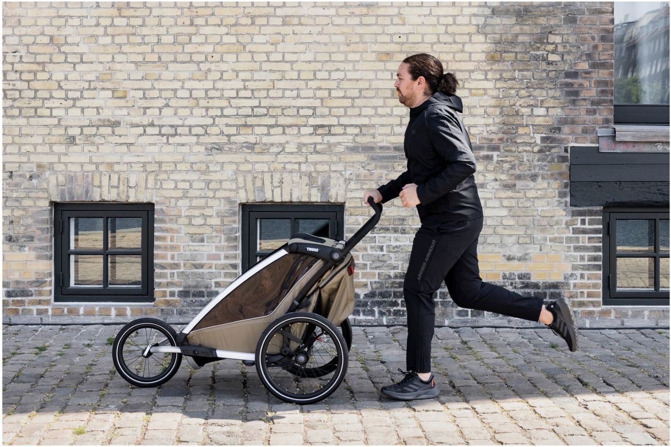 A man goes jogging with his child inside a thule bike trailler jogger with a jogging wheel.