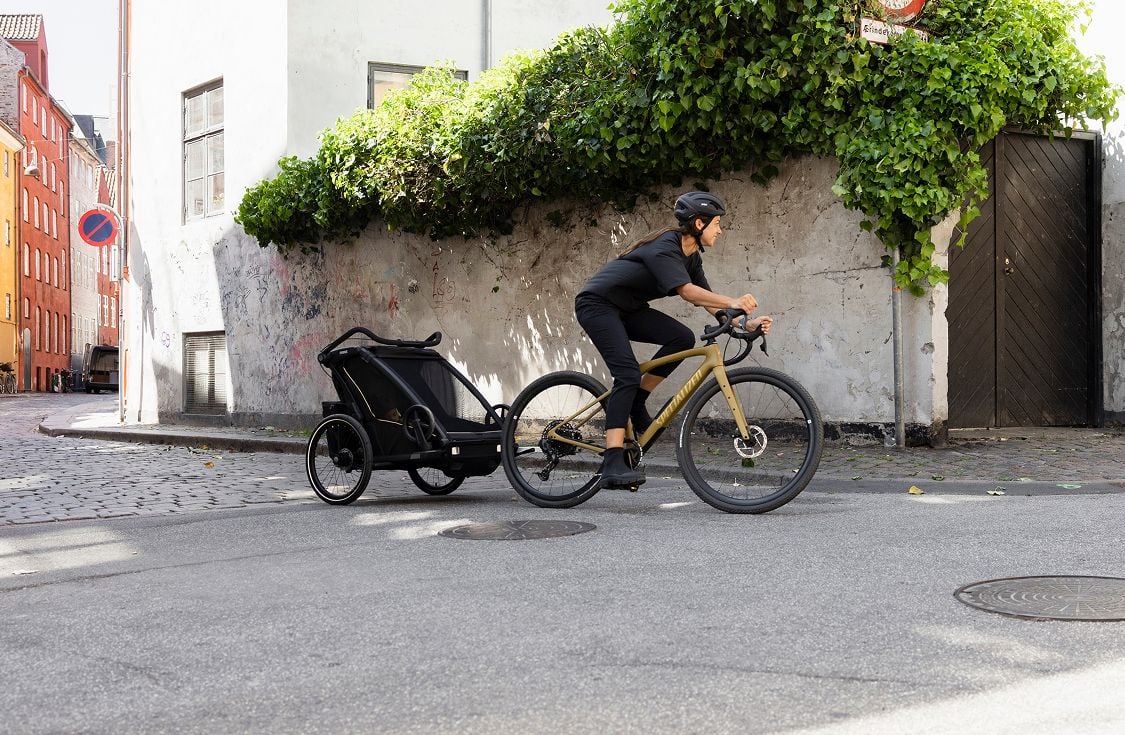 A person rides a bike while towing a child trailer on a quiet city street.