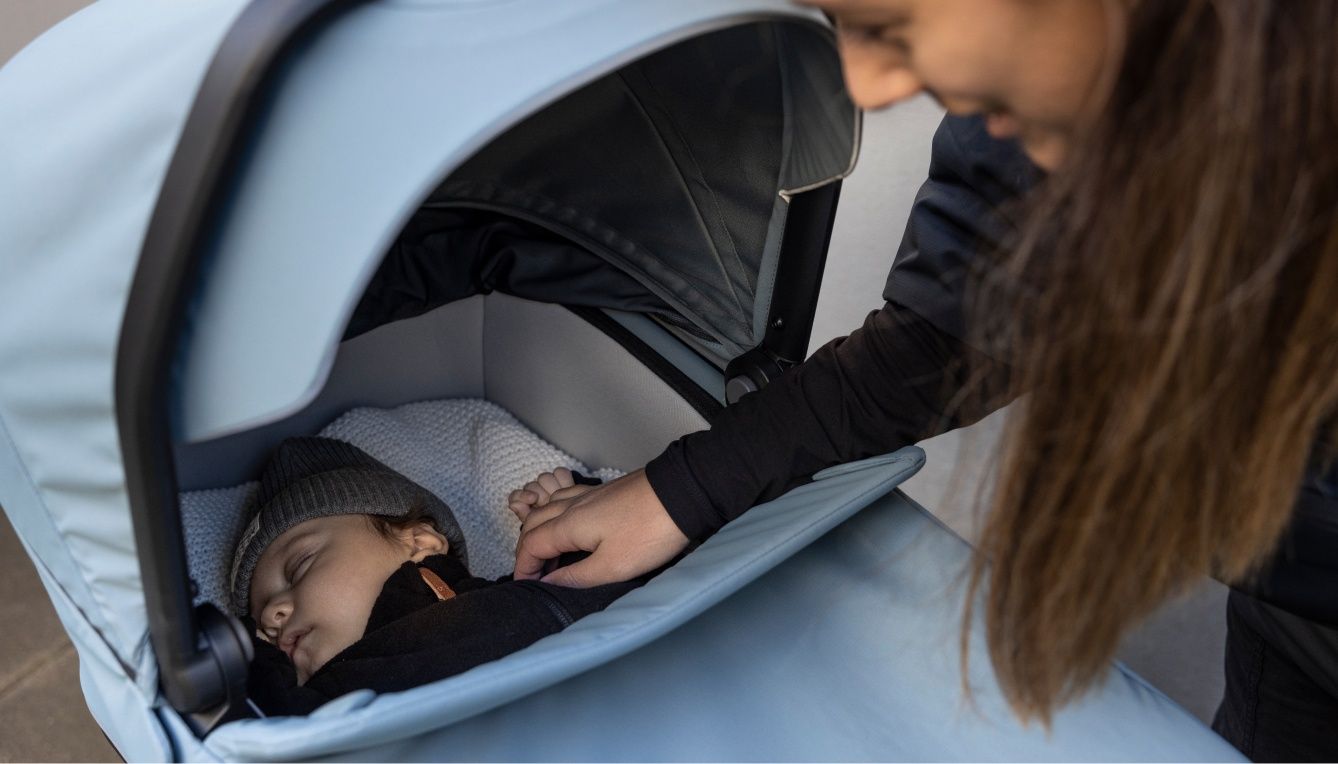 A mother observes her baby inside the bassinet of a Thule baby stroller.