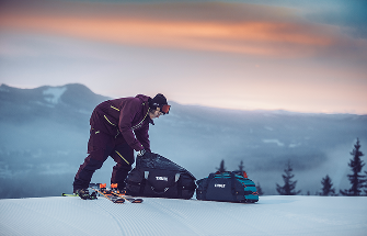 Person in Skiausrüstung, die Thule-Taschen auf einer verschneiten Piste packt.