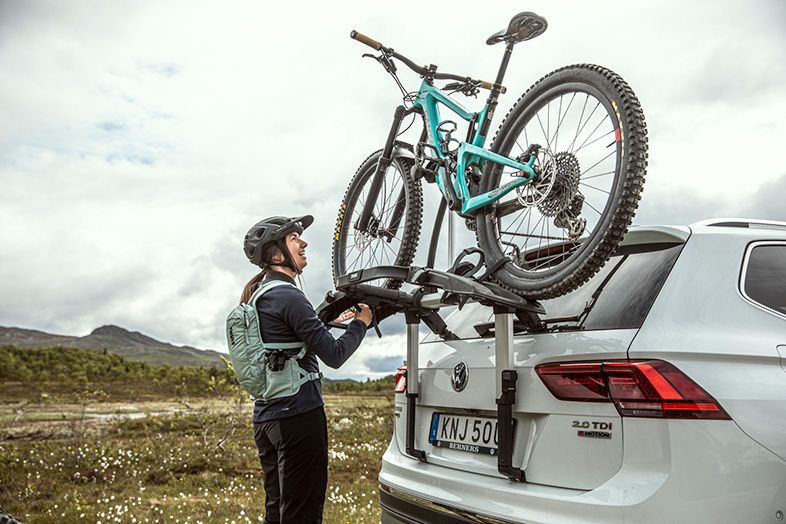 In the countryside a cyclists loads bikes onto a trunk bike rack.