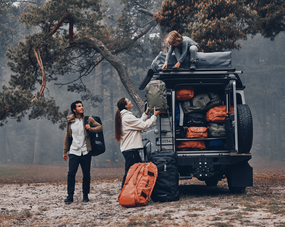 A family load their vehicle in a misty forest with Thule Chasm duffel bags.