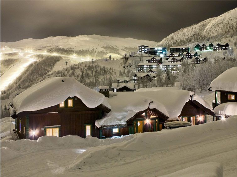 Snow-clad wood cabins at Hemsedal ski resort at night with the ski slopes lit in the background.