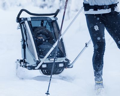 An adult pulls a Thule cross country ski carrier with a baby bundled up inside
