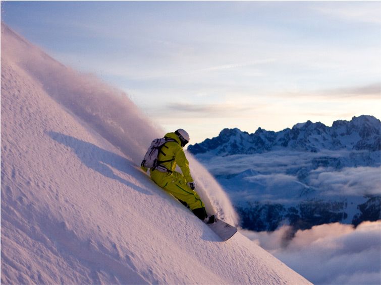A skier skis down the steep slopes at Verbier, Switzerland at dawn, with rugged peaks in the background.