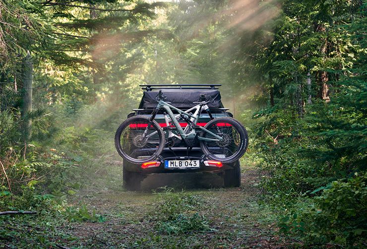 W słoneczny dzień w lesie stoi zaparkowany pojazd z bagażnikiem rowerowym Thule Epos.