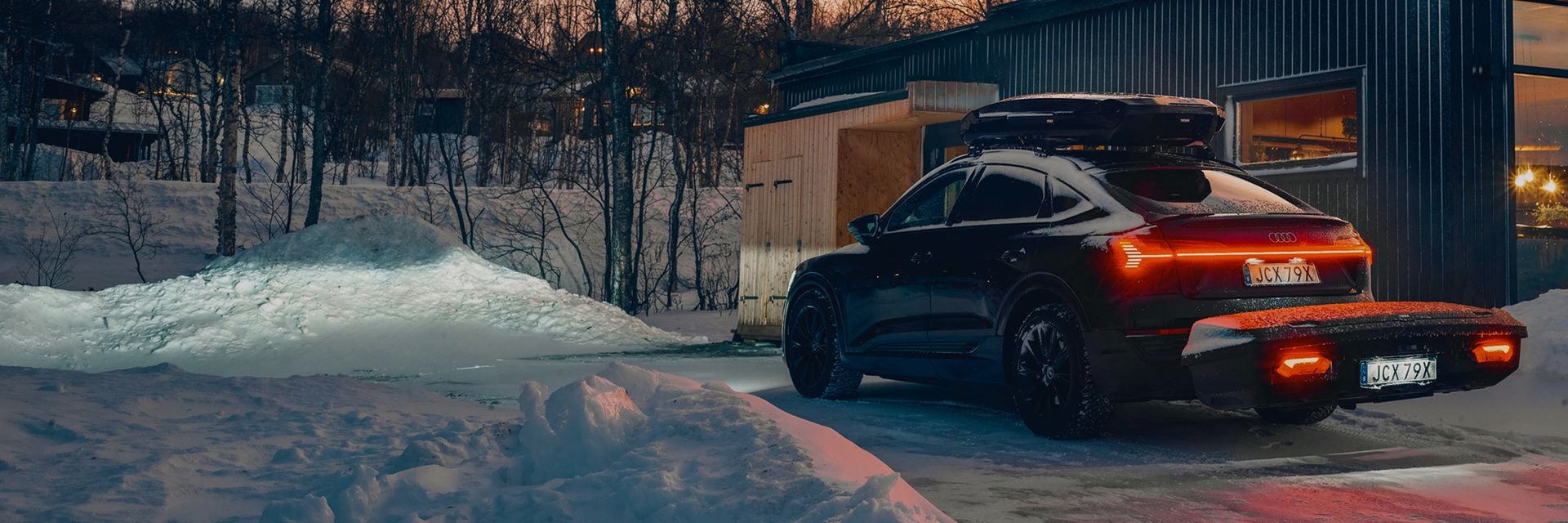 Car with Thule cargo carrier parked outside a snowy cabin at night.
