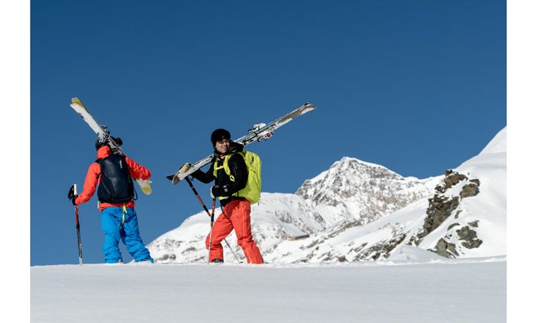 Two skiers atop a mountain with skis and Thule Upslope ski backpacks.