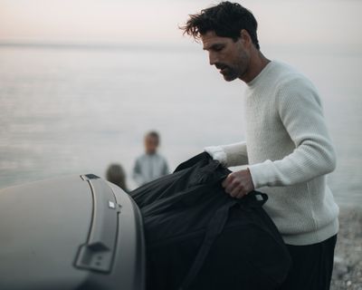 На берегу океана мужчина достает спортивную сумку из грузового бокса на фаркопе автомобиля.
