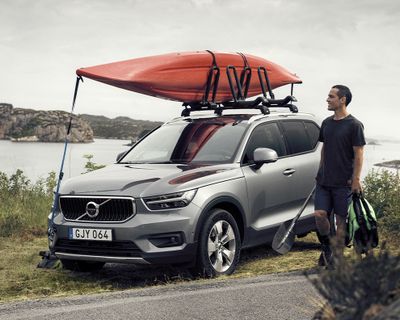 A man walks beside a parked car with a kayak on the roof racks.