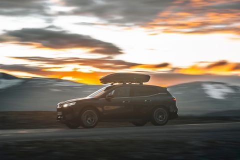 Tume auto katuse kaubakastiga, mis sõidab mööda teed.