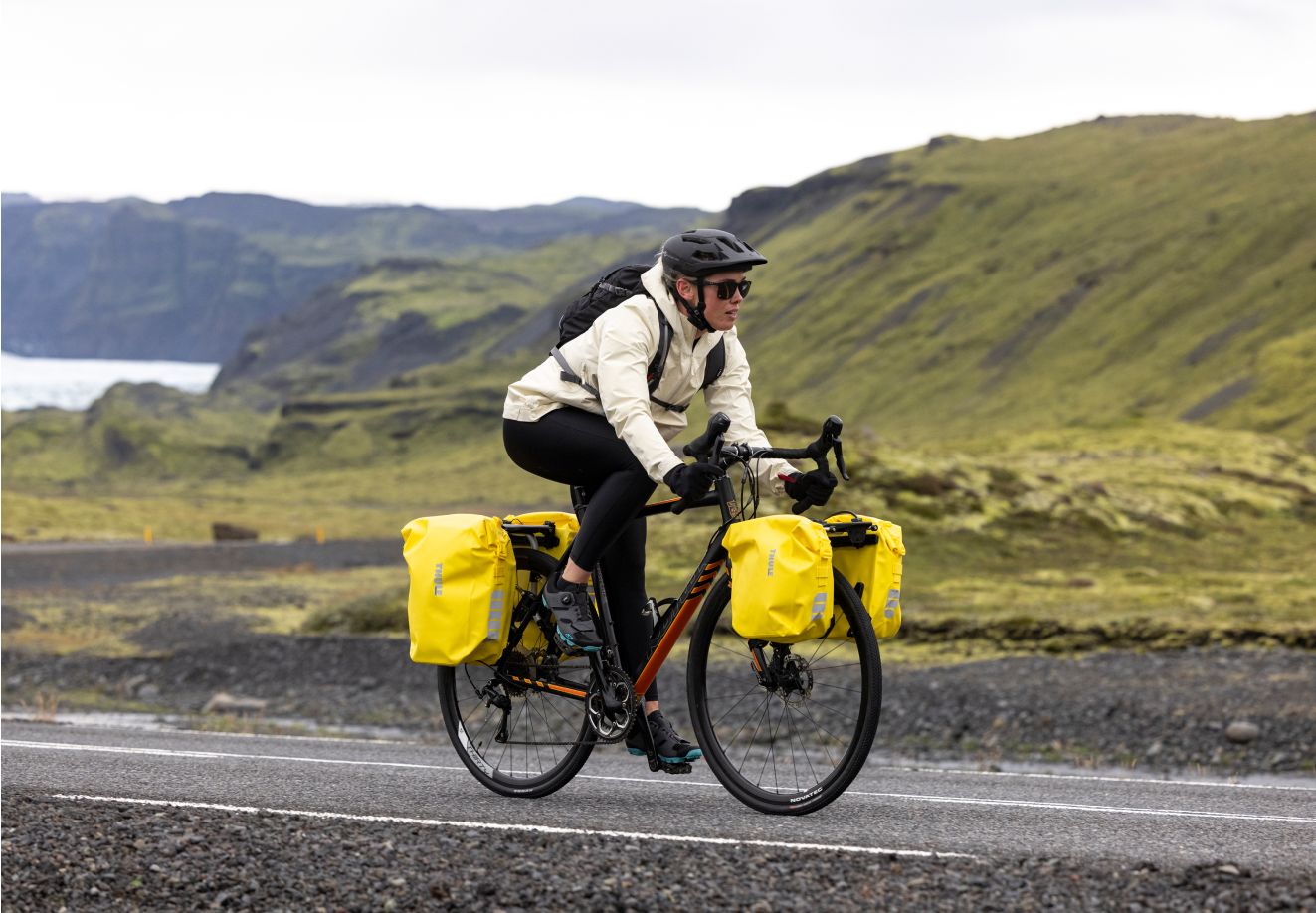 En cyklist med oppakning kører af sted i Island i barsk vejr på en landevej.