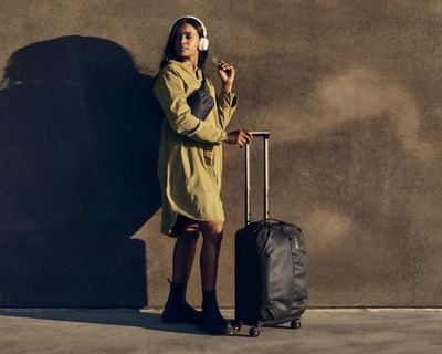 Une femme est au soleil tenant un bagage de cabine.