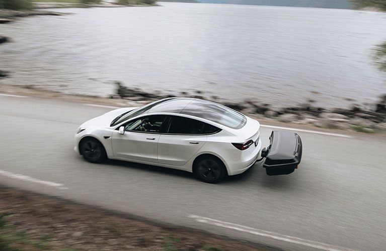 Un véhicule électrique blanc roule avec un porte-charges pour barre de traction Thule Arcos.