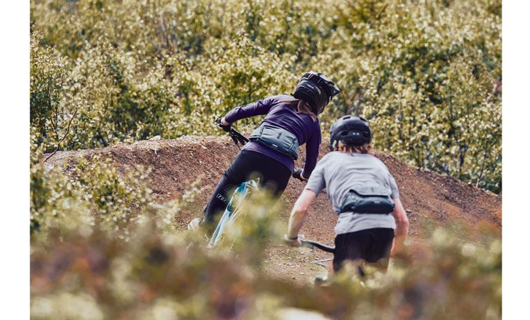 Thule mountain bikers speed down the trail with the Thule hydration pack Thule Rail Hip Pack.