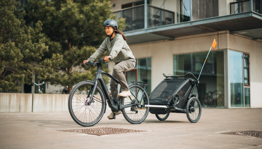 A person rides an e-bike while pulling a child trailer in a modern residential area.