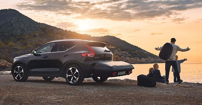 In the sunset, a family parked by the water with a car that has a Thule Arcos cargo box.