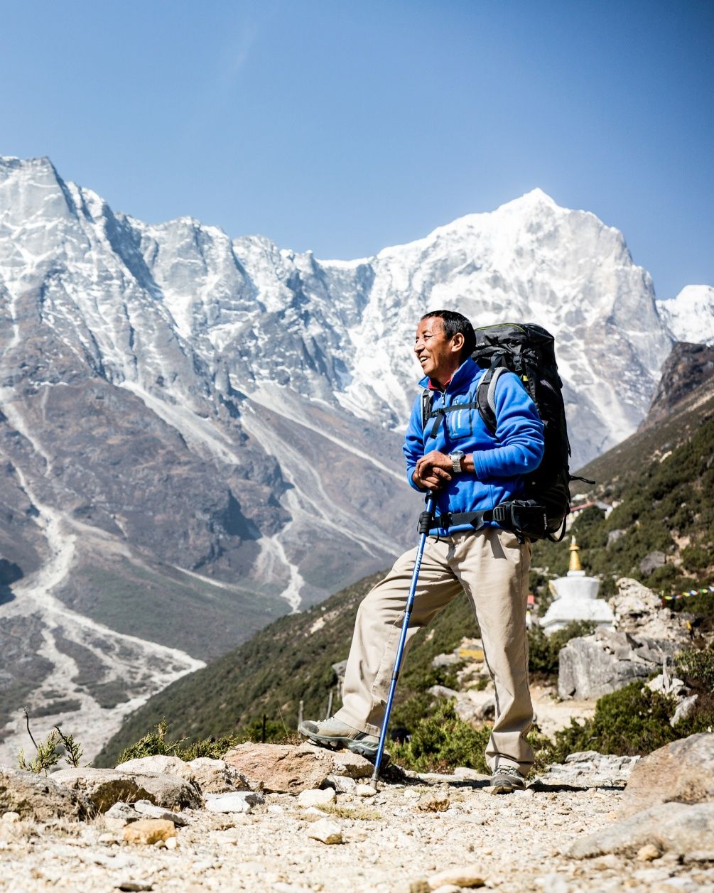 Apa Sherpa smiles while hiking with tall mountains in the background.