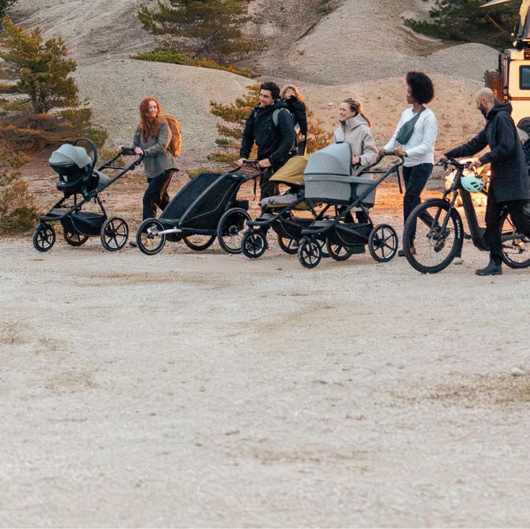 Plusieurs personnes avec des poussettes Thule marchent ensemble dans un cadre extérieur.