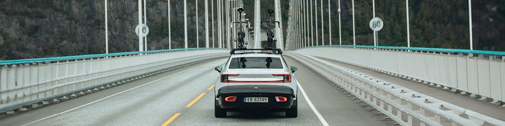 A vehicle drives over a bridge with the Thule Arcos rear cargo carrier mounted on the back.
