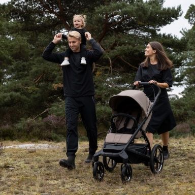 Mees, kelle õlgadel istub väikelaps, kõnnib looduses tühja lapsevankrit Thule Urban Glide lükkava naise kõrval.