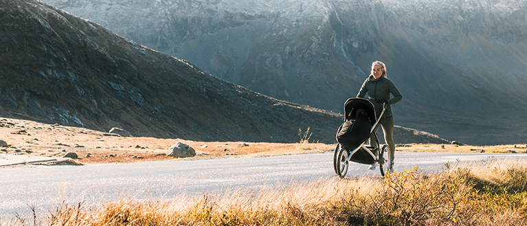 Eine Frau läuft mit einem Thule Glide Jogger-Kinderwagen durch die Landschaft.