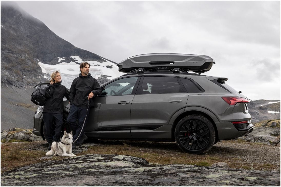 Deux personnes debout à côté d’une voiture stationnée, avec Thule Motion 3 et tenant un chien.