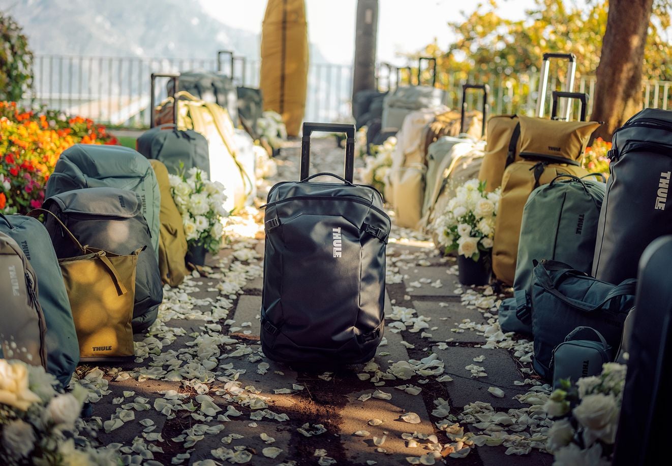 Thule Taschen säumen beide Seiten eines mit Blütenblättern übersäten Ganges, während ein schwarzes Thule Chasm Handgepäckstück vorne in der Mitte steht und auf ein lebensveränderndes Ereignis zu warten scheint.