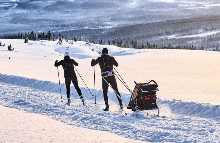 Una pareja practica esquí a campo traviesa con un Thule Chariot Sport negro y un kit de esquí de remolque de bicicletas. 