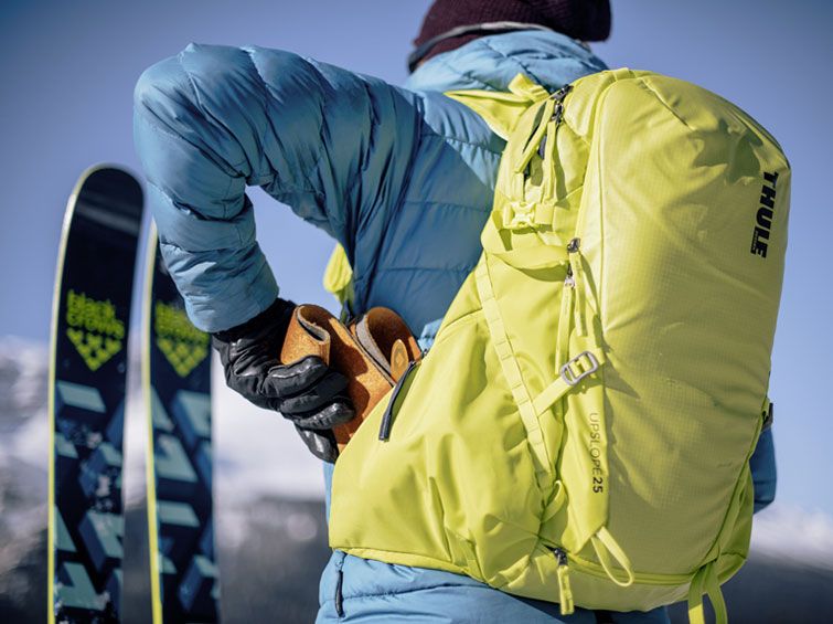 A close-up of someone putting their gear into the side pocket of one of the Thule ski and snowboard backpacks.