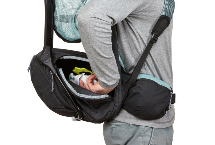 A person reaching to put something inside the pocket of the Thule Sapling child carrier backpack.