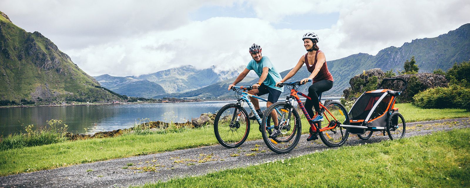 Una pareja anda en bicicleta en las montañas neblinosas con un remolque para bicicletas para niños Thule.