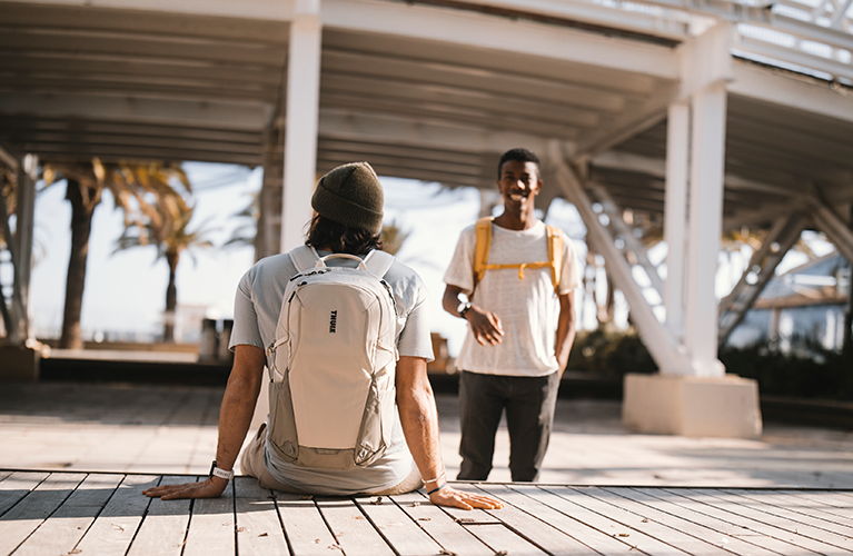 Dos estudiantes parados en un lugar soleado con palmeras mientras cargan mochilas Thule Enroute.