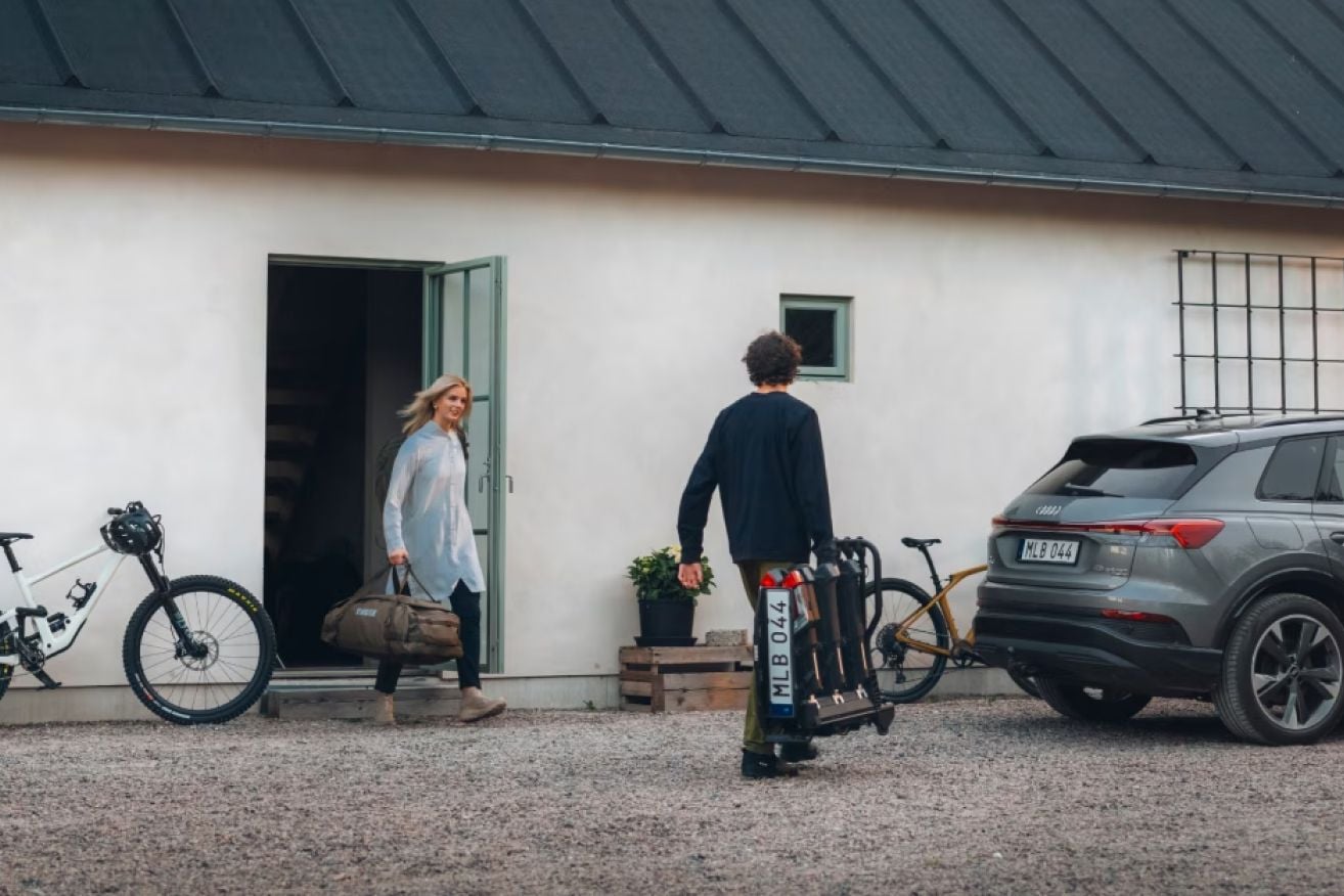 Menschen, die Motorräder vorbereiten und Thule-Ausrüstung bei einem Auto vor einem hellen Haus laden.