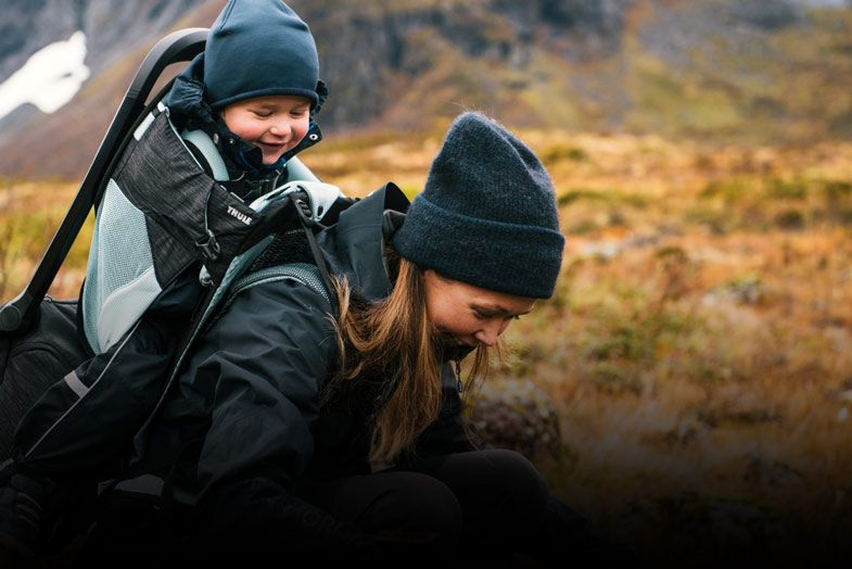 Woman hiking with a child in the child carrier backpack Thule Sapling.